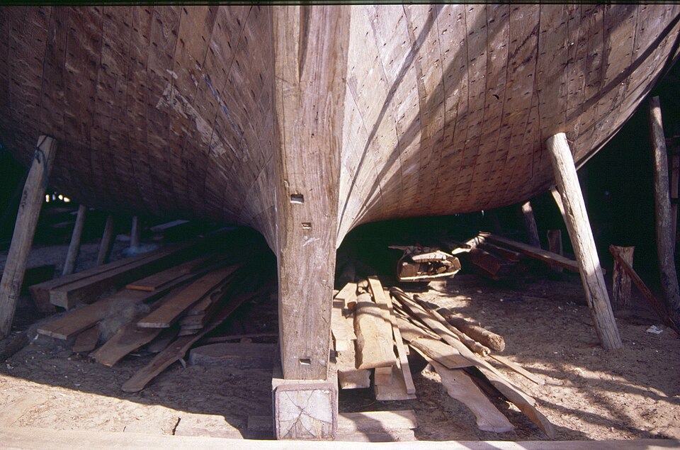 Beypore Uru under construction — showing the exposed wooden hull framework of a partially built Uru at Beypore shipyard, with the characteristic curved keel, structural ribs, and teak planking assembly that demonstrates the Khalasi and Odayi craftsmen's technique of building from memory without blueprints or modern tools