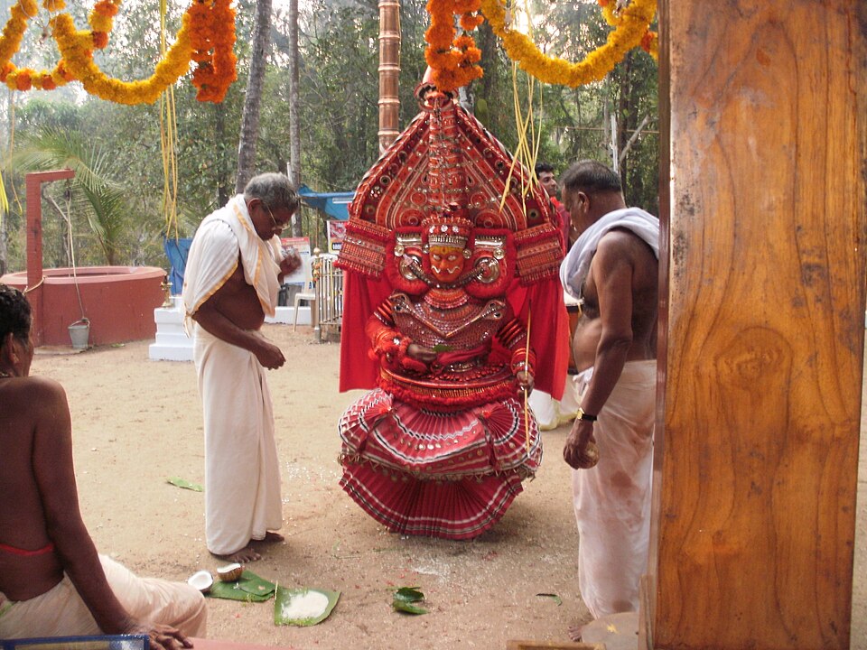 Bhairavan Theyyam performer in active ritual dance — showing the intense physical and spiritual energy of the Theyyam performance after the Mudi placement, when the deity is believed to be fully present in the performer's body, with the characteristic colours, ornaments, and physical intensity of Bhairavan's fierce manifestation