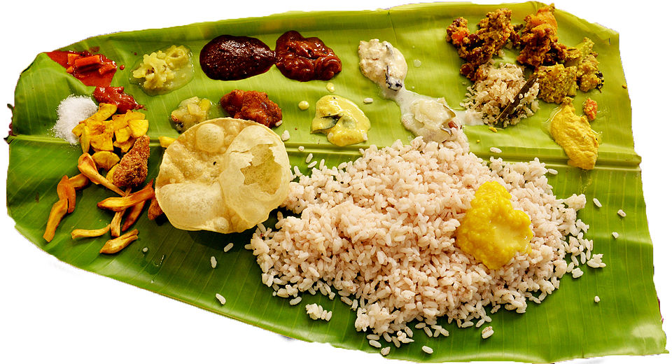 Kerala Sadya served on a banana leaf — the traditional arrangement of 20 to 26 dishes in their specific positions on the leaf, showing the full spread of a classic Sadya with rice at centre, curries to the right, condiments and snacks at top left, payasam desserts to the right of centre, and banana at far left, the complete visual articulation of Kerala's most sophisticated food tradition