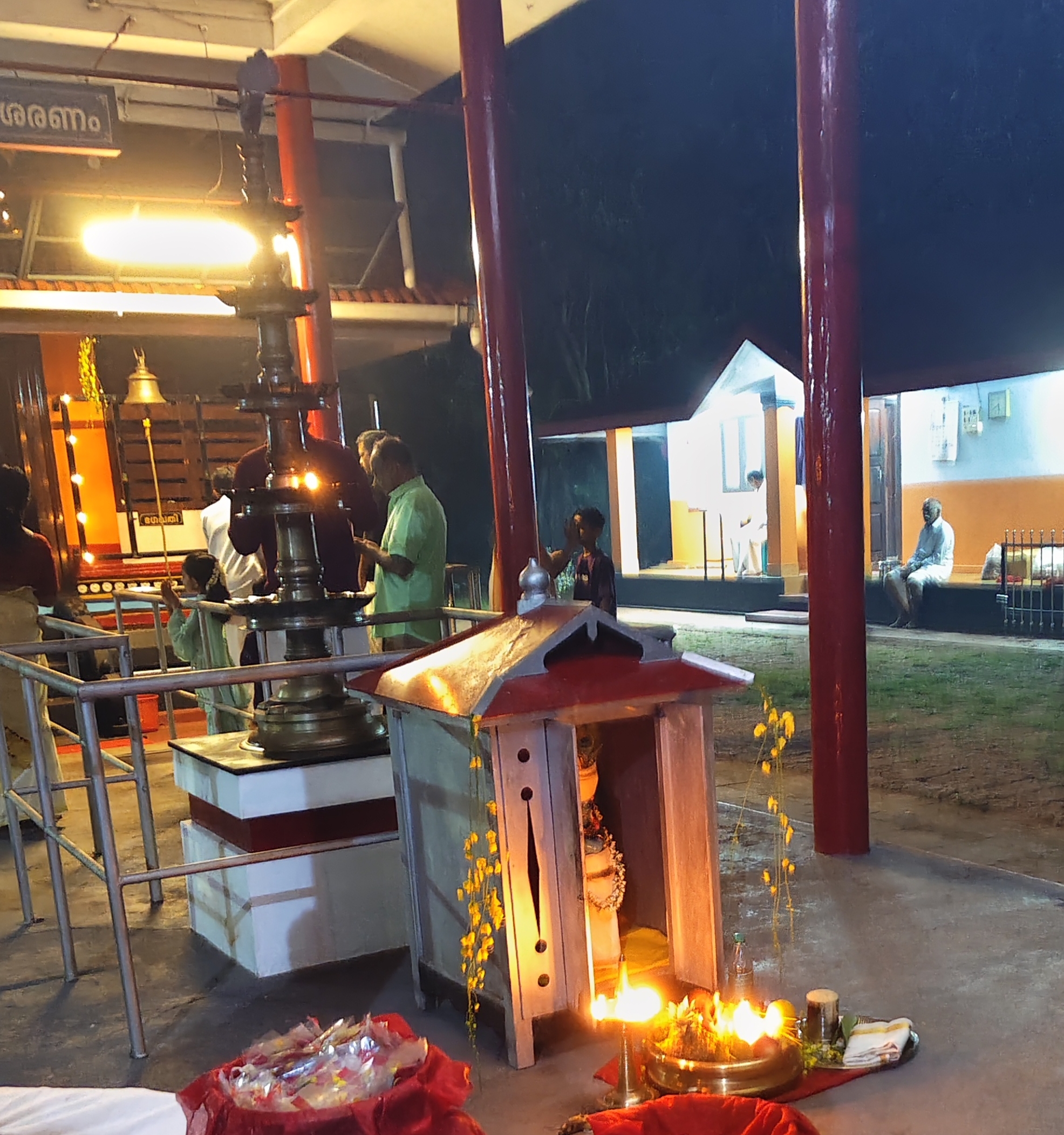 Vishukkani arranged at a local Bhagavathy temple in Kerala — the traditional arrangement of auspicious items including Kani Konna flowers, Krishna idol, lamp, fruits, and the Aranmula Kannadi mirror at a community temple shrine, showing how the Vishukkani tradition extends from family homes into the public devotional spaces of Kerala's temple culture
