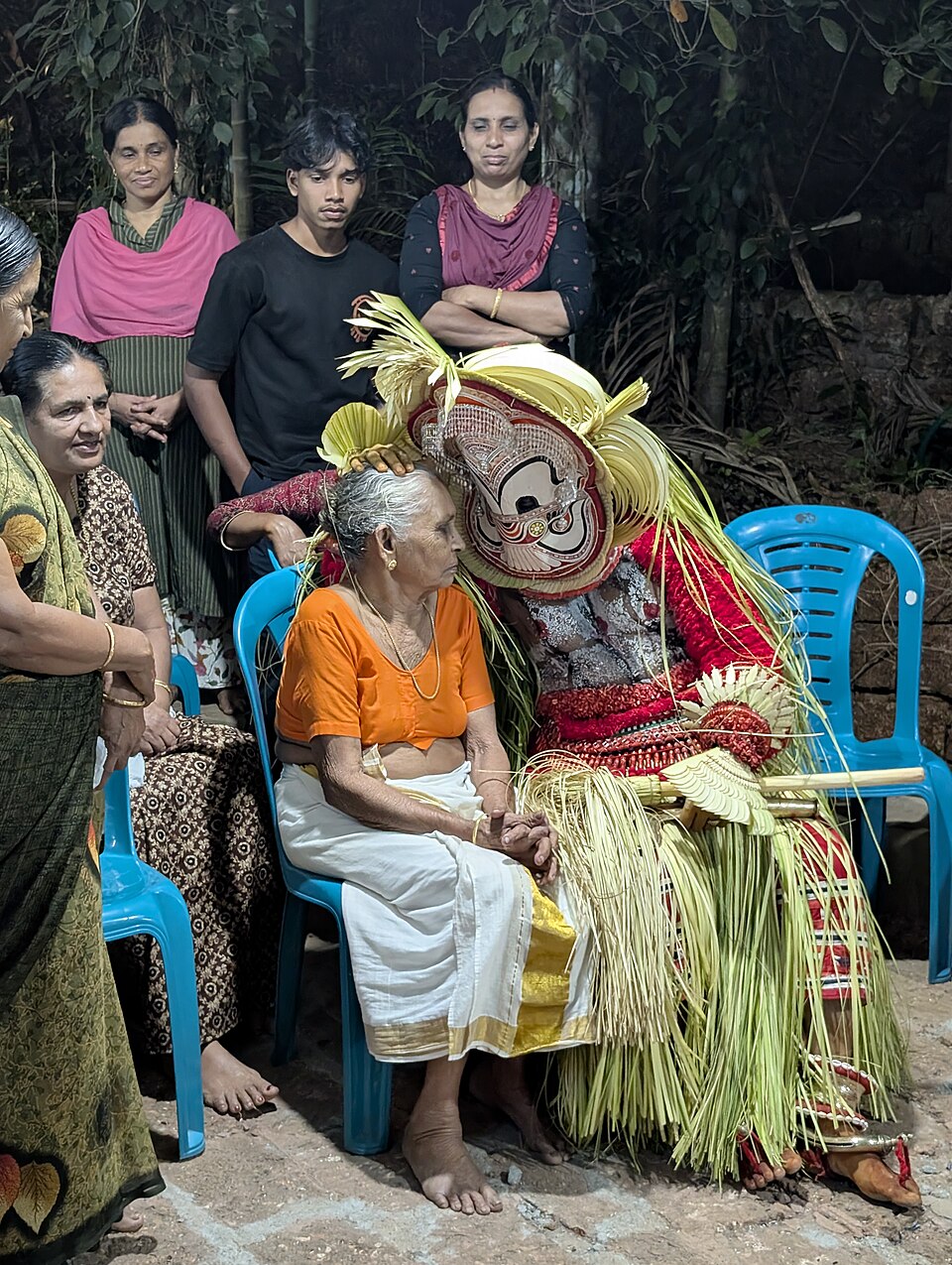 Whispers of grace — Pottan Theyyam sharing a close, affectionate moment with a grandmother at Maruthodan Tharavad, North Malabar, Kerala — the divine meeting devotion in an intimate human exchange that captures the heart of Pottan Theyyam's message: that the sacred is found in ordinary human connection, not in status or ceremony